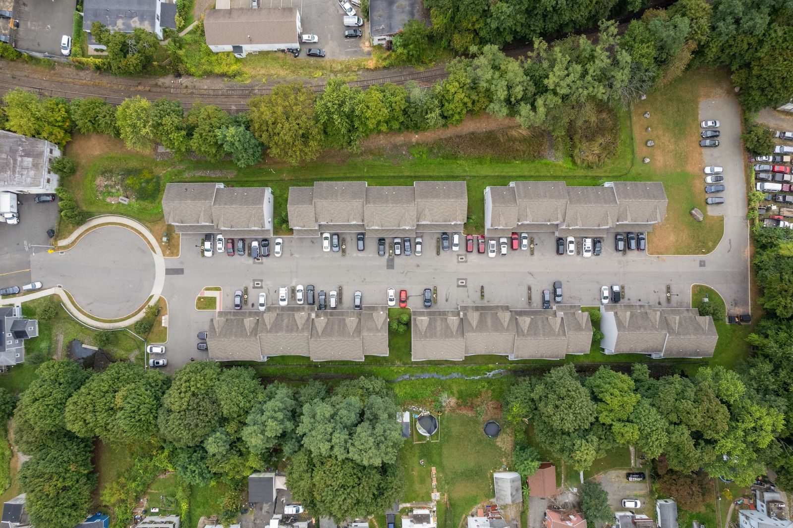 Top-down aerial of six townhome buildings facing each other across a shared drive, surrounded by trees