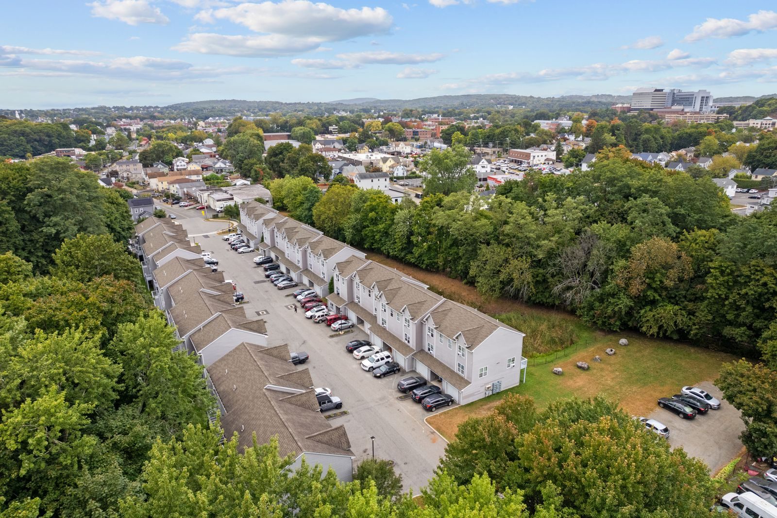 Aerial view of the two rows of townhomes along a tree-lined drive, with Danbury and its hills in the distance